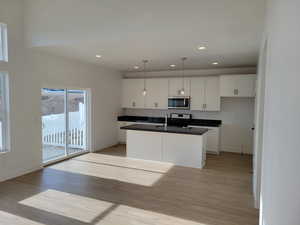 Kitchen with natural light, microwave, range oven, pendant lighting, light hardwood flooring, dark countertops, and white cabinetry