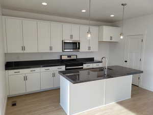 Kitchen with wood-type flooring, microwave, range oven, white cabinets, pendant lighting, and dark stone countertops