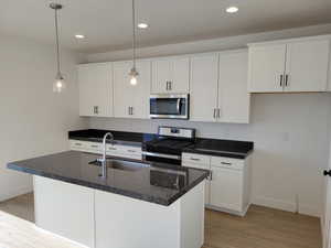 Kitchen featuring microwave, gas range oven, white cabinets, pendant lighting, dark stone countertops, and light parquet floors