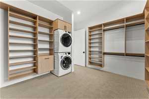 Laundry room with light colored carpet, cabinets, and stacked washer / drying machine