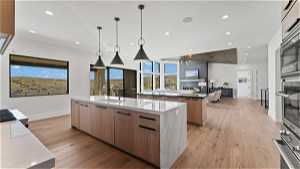 Kitchen featuring sink, decorative light fixtures, a fireplace, light hardwood / wood-style floors, and a kitchen island with sink
