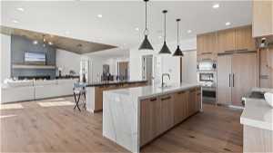 Kitchen with light hardwood / wood-style floors, sink, an island with sink, a fireplace, and light stone counters