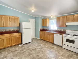 Kitchen featuring natural light, refrigerator, range hood, gas range oven, dishwasher, light tile floors, dark countertops, and brown cabinetry