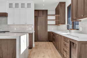 Kitchen with sink, light hardwood / wood-style floors, light stone countertops, white cabinets, and beverage cooler