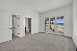 Unfurnished bedroom with ensuite bathroom, a walk in closet, access to outside, and light colored carpet