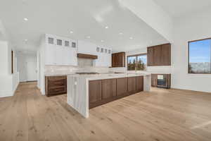 Kitchen with white cabinetry, a spacious island, decorative backsplash, and light hardwood / wood-style flooring