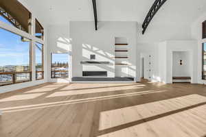 Unfurnished living room featuring beam ceiling, a towering ceiling, and light hardwood / wood-style floors