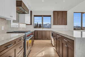 Kitchen with custom exhaust hood, double oven range, a mountain view, light stone countertops, and white cabinets