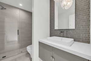 Bathroom featuring vanity, tasteful backsplash, a shower with door, and toilet