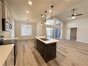 Kitchen with light wood-type flooring, ceiling fan with notable chandelier, appliances with stainless steel finishes, decorative light fixtures, and sink