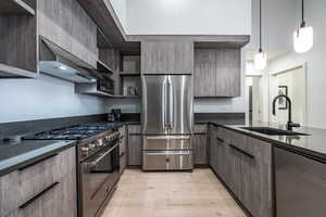 Kitchen featuring sink, appliances with stainless steel finishes, dark stone countertops, decorative light fixtures, and light wood-type flooring