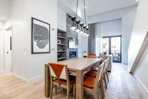 Dining space with light hardwood / wood-style floors, a tiled fireplace, a towering ceiling, and built in features