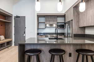 Kitchen with pendant lighting, light hardwood / wood-style floors, a kitchen breakfast bar, and stainless steel appliances