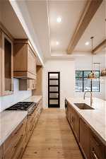 Kitchen with sink, pendant lighting, beamed ceiling, premium range hood, and light wood-type flooring