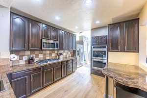 Kitchen featuring appliances with stainless steel finishes, decorative backsplash, dark brown cabinetry, and light hardwood / wood-style flooring