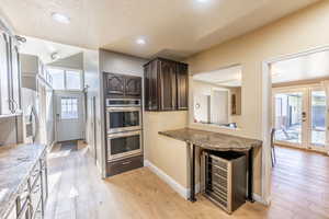 Kitchen featuring beverage cooler, appliances with stainless steel finishes, dark brown cabinetry, and light hardwood / wood-style floors