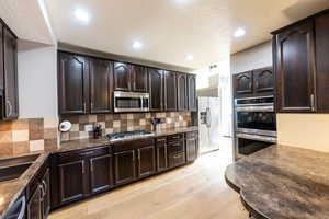 Kitchen featuring stainless steel appliances, a textured ceiling, backsplash, dark brown cabinets, and light hardwood / wood-style flooring