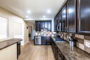 Kitchen with tasteful backsplash, light wood-type flooring, appliances with stainless steel finishes, a textured ceiling, and sink