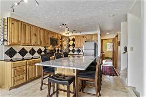 Kitchen with a kitchen bar, stainless steel microwave, light tile floors, and brown cabinets