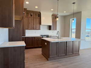 Kitchen featuring custom range hood, sink, decorative light fixtures, a kitchen island with sink, and a textured ceiling