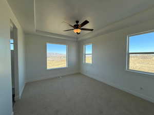 Spare room featuring ceiling fan, light colored carpet, a textured ceiling, and a tray ceiling