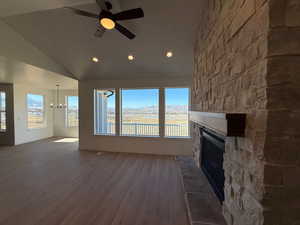 Unfurnished living room featuring ceiling fan with notable chandelier, a fireplace, a mountain view, vaulted ceiling, and hardwood / wood-style flooring