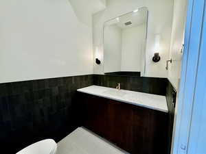 Powder room featuring tile patterned floors, vanity, toilet, and tile walls