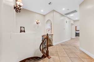 Corridor with arched walkways, light tile patterned flooring, recessed lighting, and an upstairs landing