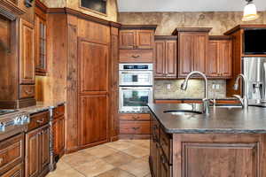 Kitchen featuring stainless steel appliances, decorative backsplash, light tile patterned floors, sink, and a kitchen island with sink