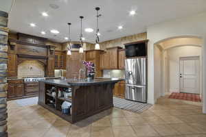 Kitchen with light tile patterned flooring, decorative light fixtures, stainless steel fridge with ice dispenser, an island with sink, and a breakfast bar area