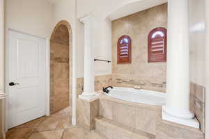 Bathroom featuring ornate columns, a bath, and stone tile flooring