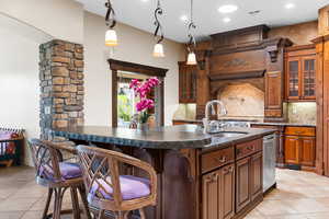 Kitchen featuring light tile patterned floors, backsplash, glass insert cabinets, a breakfast bar area, and recessed lighting