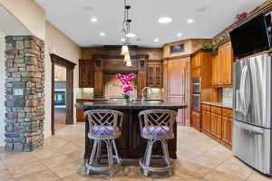 Kitchen featuring stainless steel appliances, a center island with sink, brown cabinets, light tile patterned floors, and recessed lighting