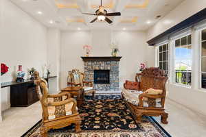 Living area with carpet flooring, coffered ceiling, beam ceiling, a ceiling fan, and a stone fireplace