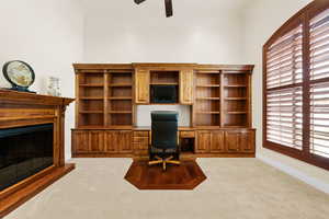 Carpeted home office with a ceiling fan, built in study area, and a glass covered fireplace