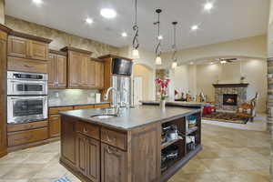 Kitchen featuring appliances with stainless steel finishes, a stone fireplace, an island with sink, pendant lighting, and sink