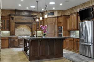 Kitchen featuring a center island with sink, dark stone countertops, hanging light fixtures, tasteful backsplash, and appliances with stainless steel finishes