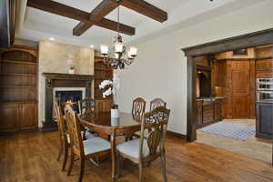 Dining area featuring coffered ceiling, an inviting chandelier, beamed ceiling, dark hardwood / wood-style floors, and a fireplace