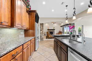 Kitchen featuring arched walkways, ceiling fan, a fireplace, appliances with stainless steel finishes, and decorative backsplash