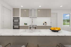 *Virtually Staged* Kitchen featuring double oven, ventilation hood, range oven, and light stone countertops