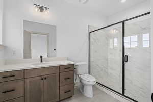 Full bathroom with tile floors, toilet, mirror, vanity with extensive cabinet space, and enclosed shower