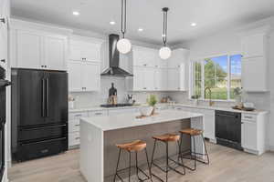 Kitchen featuring a breakfast bar, natural light, a kitchen island, stainless steel dishwasher, refrigerator, exhaust hood, gas cooktop, white cabinets, pendant lighting, light countertops, and light hardwood flooring