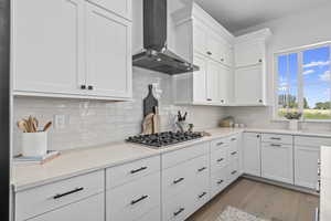 Kitchen featuring hardwood flooring, stainless steel finishes, extractor fan, gas stovetop, light countertops, and white cabinetry