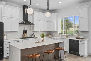 Kitchen with hardwood flooring, a breakfast bar area, natural light, a kitchen island, ventilation hood, dishwasher, gas stovetop, pendant lighting, light countertops, and white cabinetry