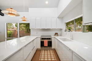 Kitchen with natural light, electric cooktop, oven, white cabinets, light flooring, light countertops, and pendant lighting