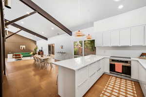 Kitchen with beamed ceiling, natural light, electric stovetop, oven, white cabinets, pendant lighting, light floors, and light countertops