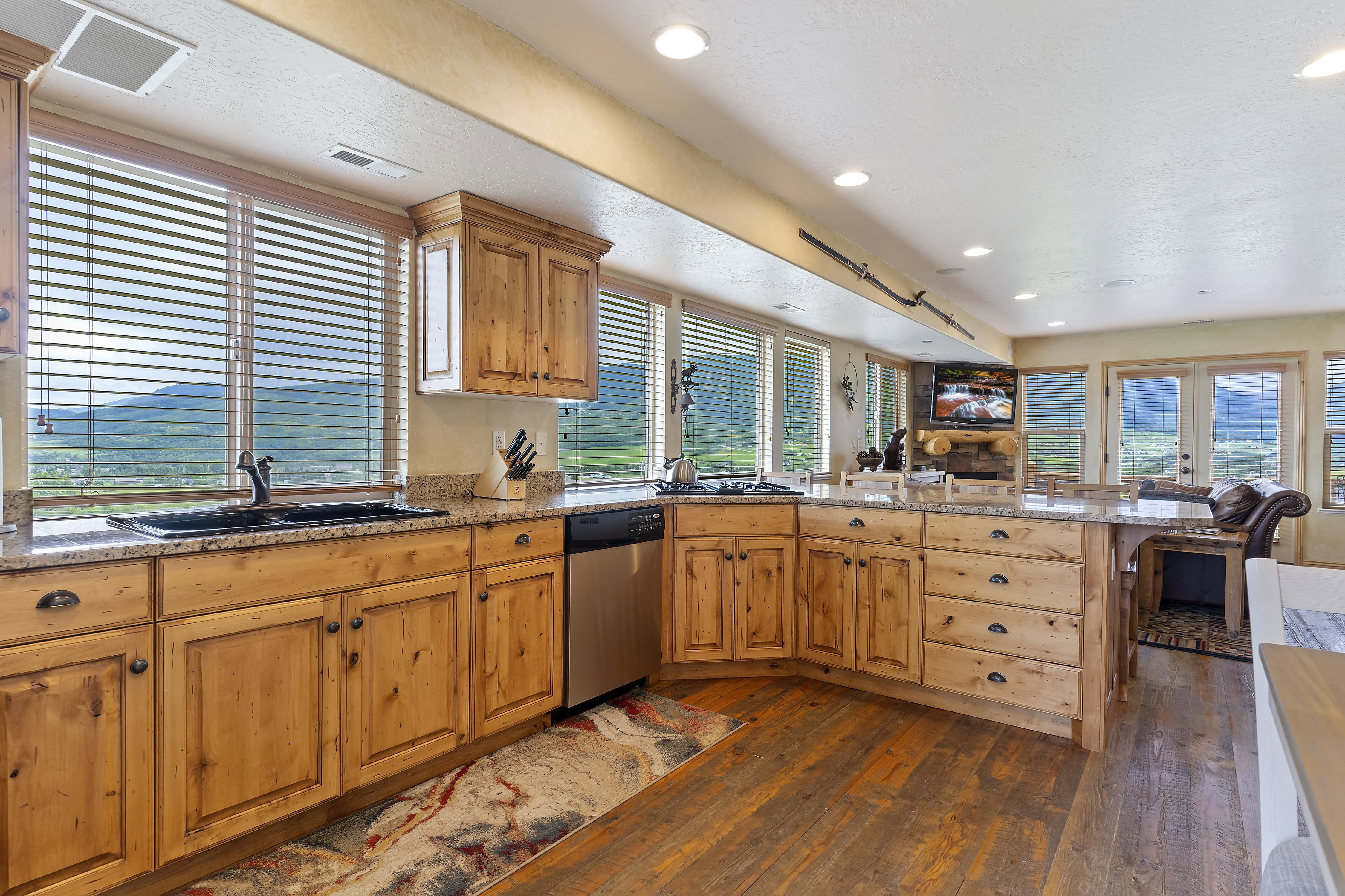 Kitchen with natural light, TV, stainless steel dishwasher, brown cabinets, and dark hardwood flooring