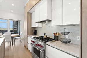 Kitchen featuring natural light, stainless steel finishes, gas range oven, white cabinets, light countertops, and light parquet floors