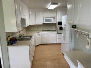 Kitchen with microwave, electric stovetop, oven, white cabinets, light hardwood floors, and light countertops