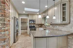 Kitchen with skylight, stainless appliances, pendant lighting, white cabinetry and granite countertops
